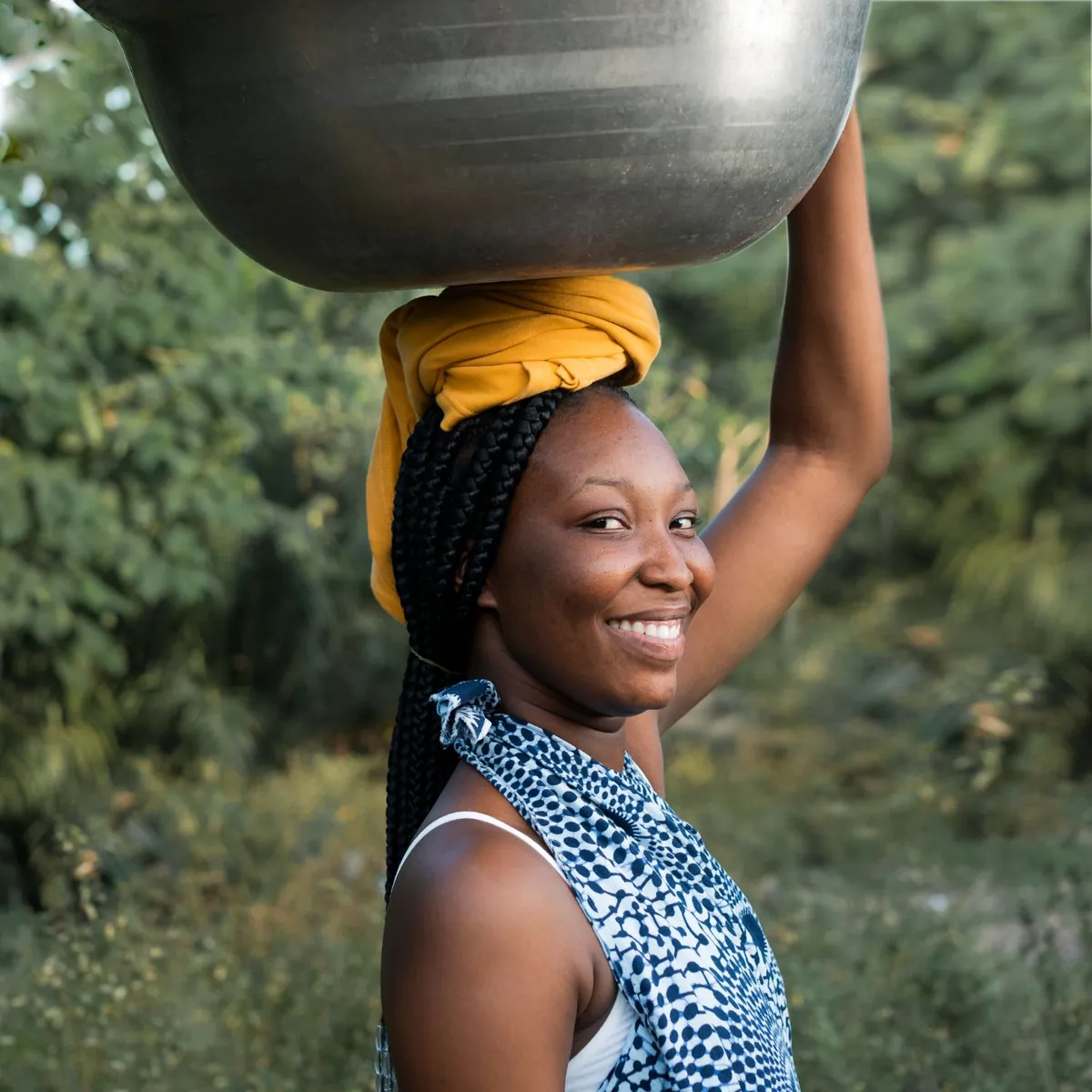 A woman is carrying a large bowl on her head.